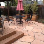 A patio with a table and chairs, umbrella and plants.