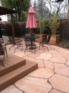 A patio with a table and chairs, umbrella and plants.